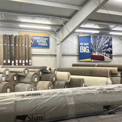 Large Shaw plastic-wrapped carpet roll in a warehouse with stacked neutral rolls below